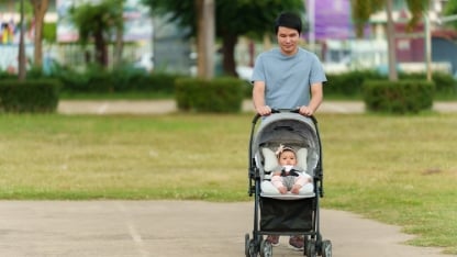 happy father pushing infant baby stroller and walking in the park