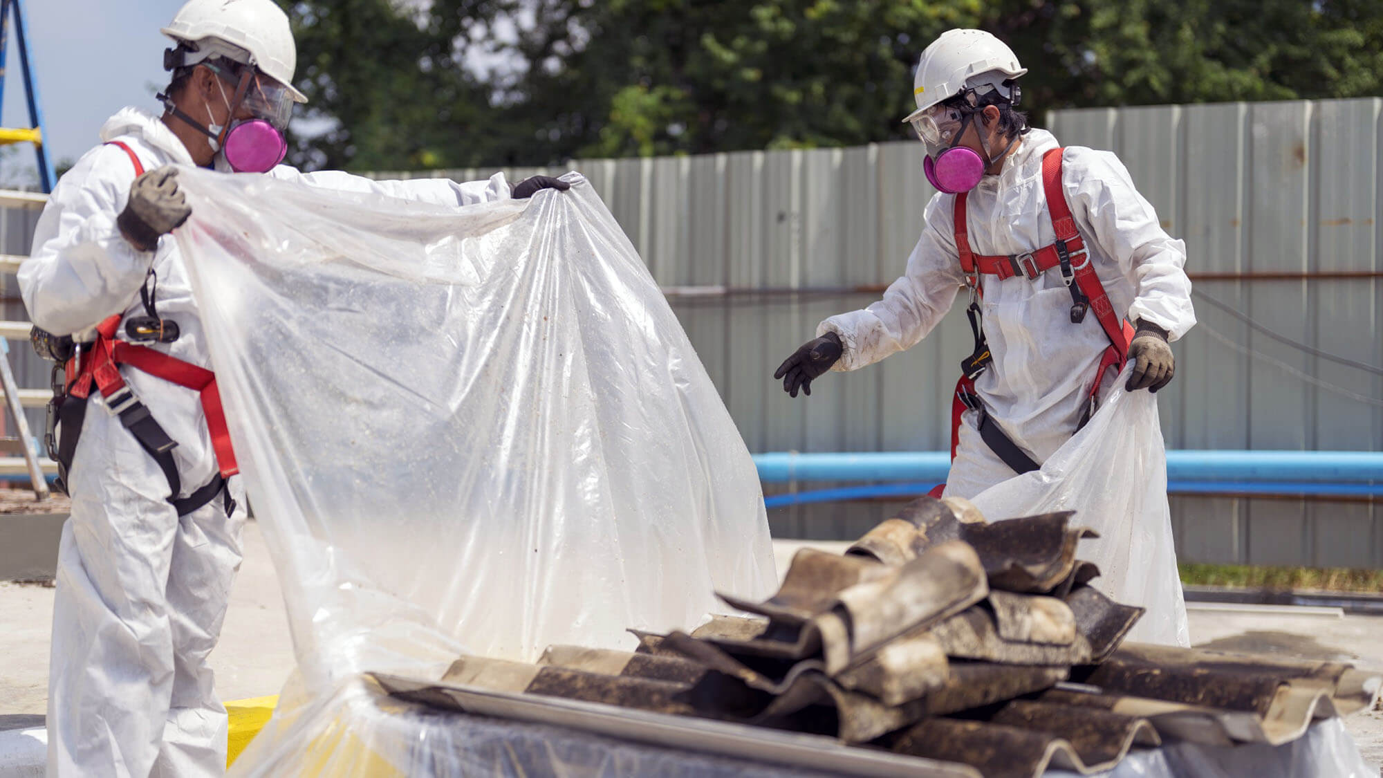 Workers wearing full body protective clothing while working with the asbestos roof tiles. Hazardous waste management and working safety concept. Professional waste disposal.