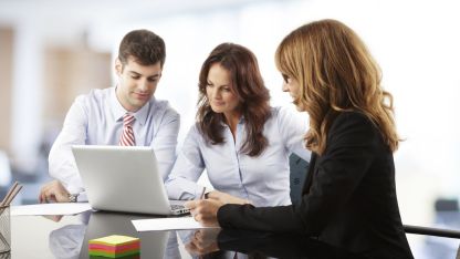 Business professionals reviewing information together on a laptop during a meeting.