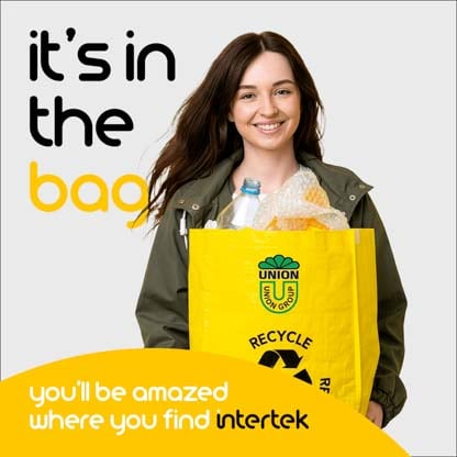 A woman smiling while carrying a bag full of recyclable content